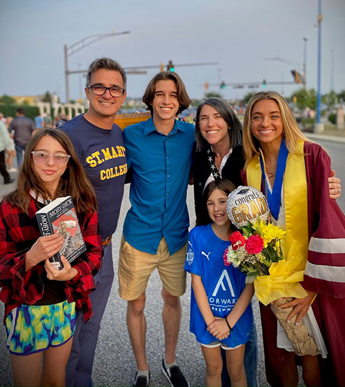 Arizzi family photo featuring the dad, his wife, son and three daughters, one of which is dressed in graduation attire and holding a balloon and flowers.