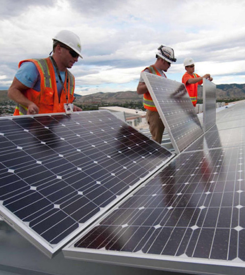 photo of men with hard hats and orange vests working on solar panels