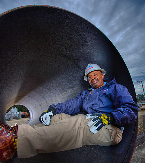 male worker with a hard hat sits inside industrial sized pipe
