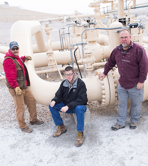 three male workers standing in front of large industrial plumbing/valve system