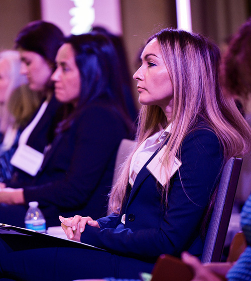 Woman sitting at the Military Spouse Employment Summit next to other women listening to a speaker.