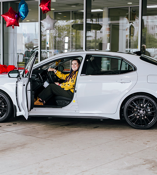 Toyota Sweepstakes winner smiling, sitting in her new car with the door open.