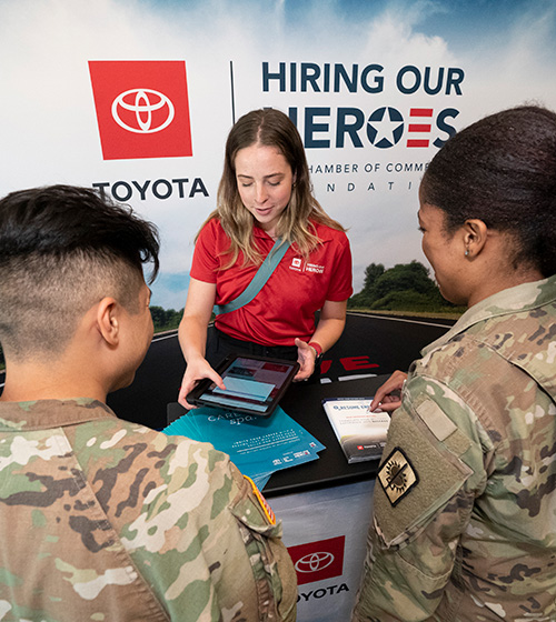 A representative for Toyota speaks with service members in uniform.