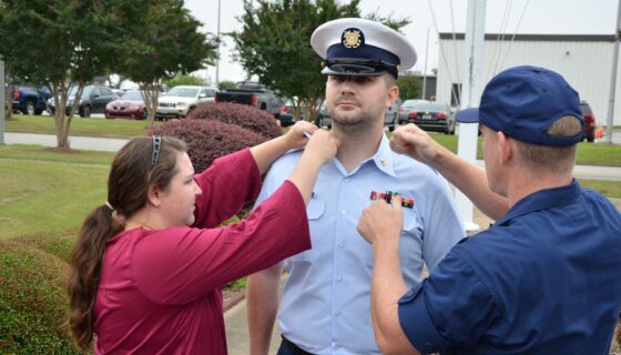 Photo of U.S. Coast Guard veteran Rhys Campbell with two people adding pins to his uniform