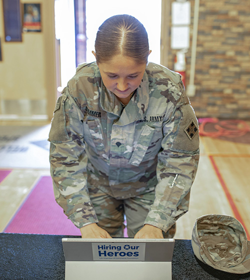 Service member typing on a computer with a Hiring Our Hereos logo on back.