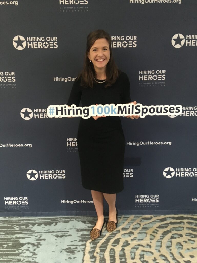Navy spouse Allison Gunta holds a #HOH100kMilSpouse sign at a Hiring Our Heroes event.