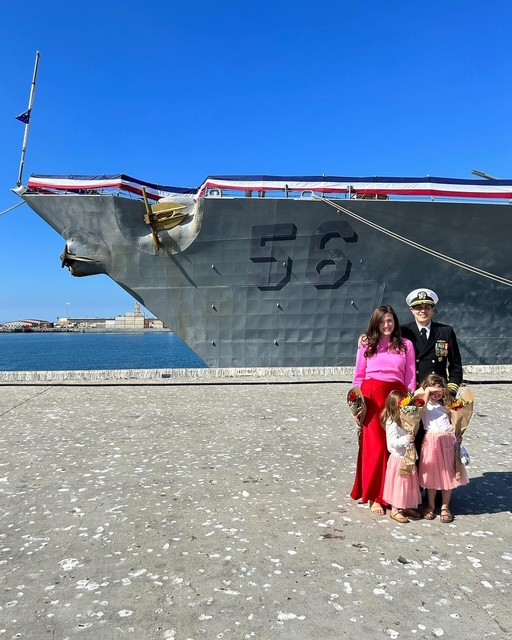 Allison Gunta, a U.S. Navy spouse, standing with her family in front of a Navy ship, symbolizing their military journey and resilience