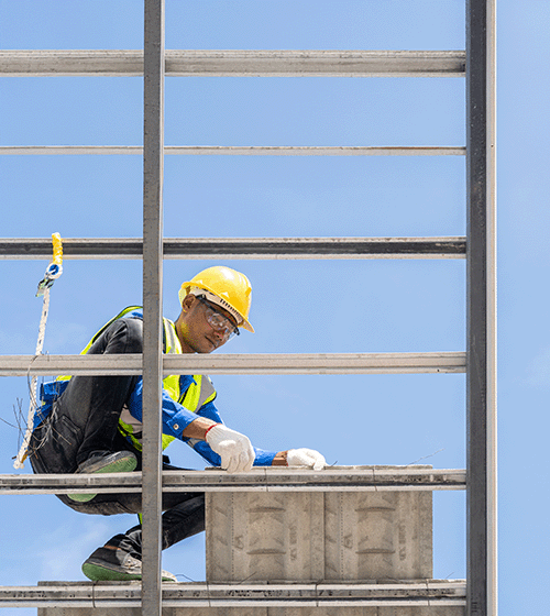 A construction worker wearing a yellow hard hat and safety gear works on a roof.
