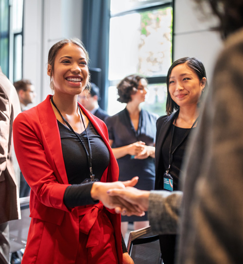 woman in a professional red outfit smiling and shaking hands with potential employer