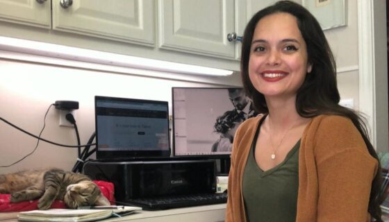 Karen Uhlhorn sitting at her remote workstation in her house with her trusty co-worker (and cat) – Petrus.