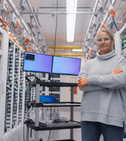 woman folding her hands standing in front of computer screens and data center equipment