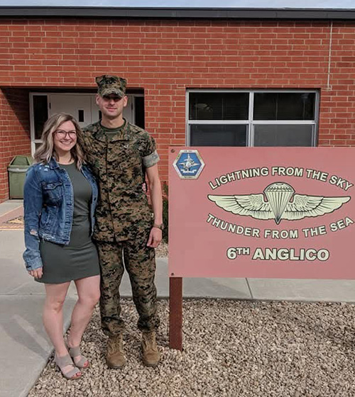 Savana Dempich, military spouse, poses with her uniformed husband next to the Lightning from the Sky, Thunder from the Sea 6th Anglico sign.