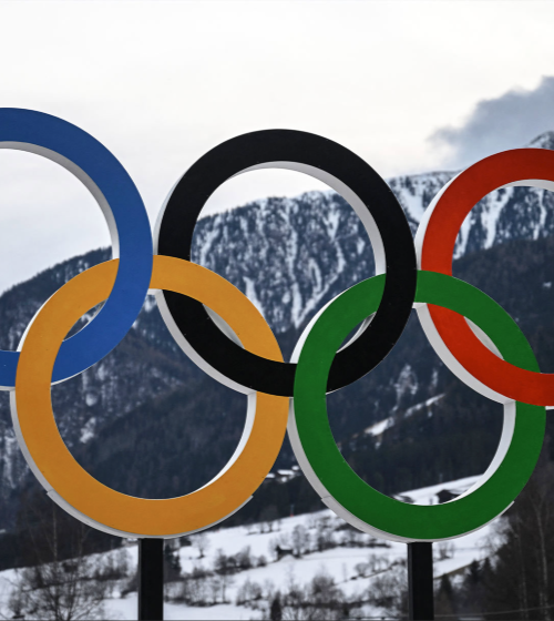 Photo of Olympic rings with a snowy mounting in the background.