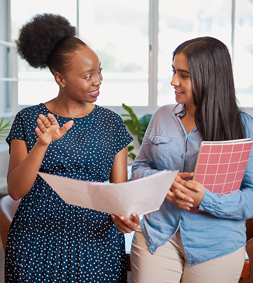 Two women speak with each other where one is explaining to the other.