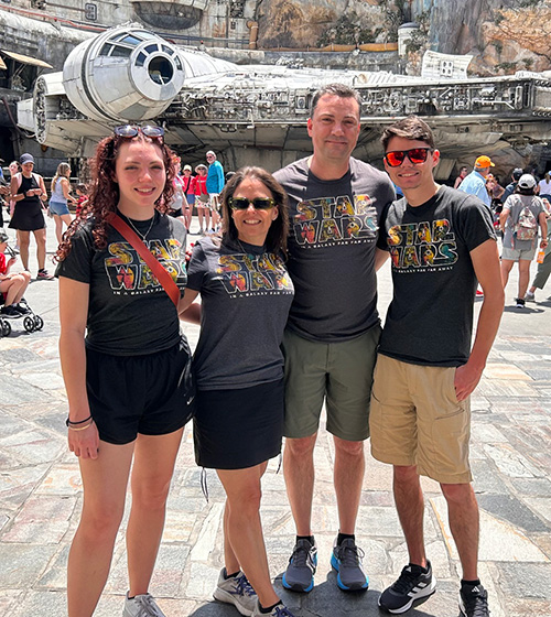 John Melendez poses for a photo with his family, all wearing Star Wars shirts, in front of an exhibit of the Millennium Falcon, the most famous of all rebel starships in the Star Wars universe.