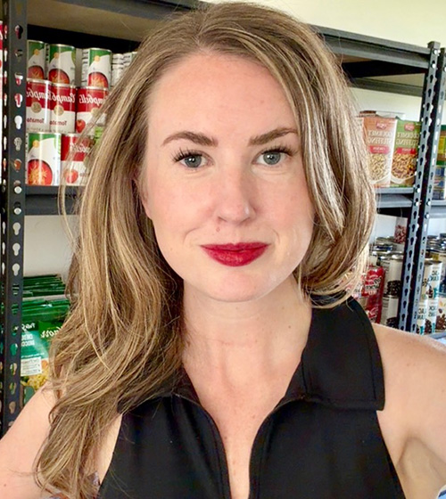 Close up of Megan Rowley standing in front of shelves of food at the JBAB food pantry.
