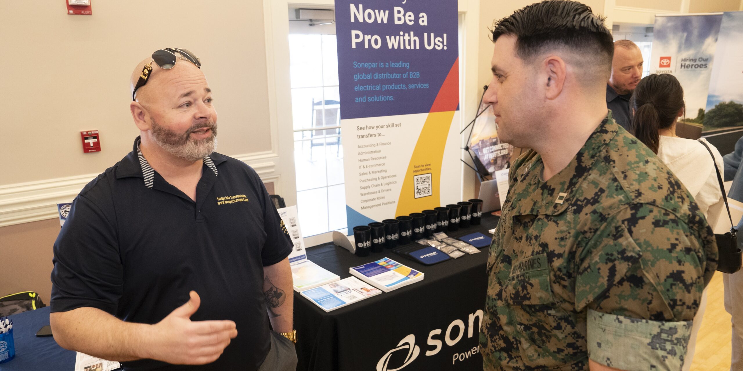 A marine talking to an employer in front of a hiring fair booth.