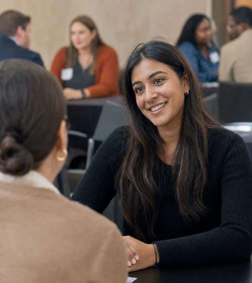 Two women speak in a professional networking setting.