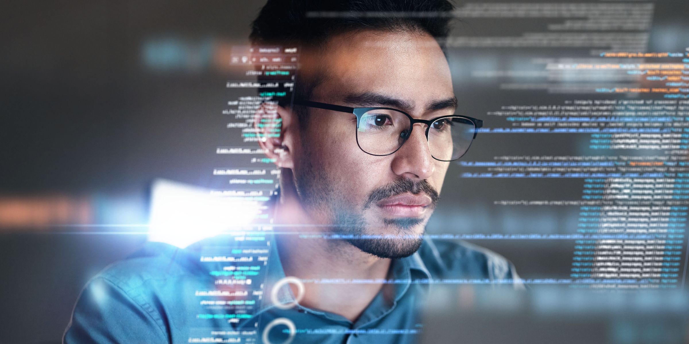 A serious man with glasses looks at a computer with data superimposed over the image.