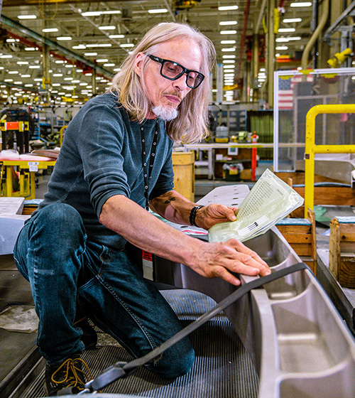 man wearing eye protection, working on a metal project in a manufacturing facility