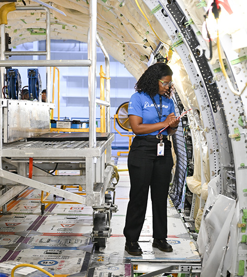 Female Boeing employee in an aerospace manufacturing facility writing on a clipboard
