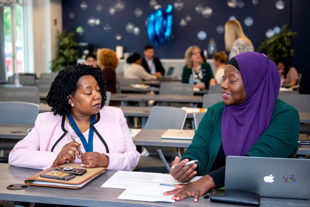 Two women sit at a table going over materials together.