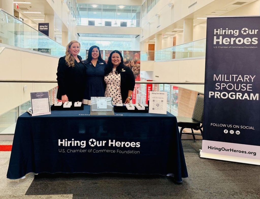 Three Hiring Our Heroes employees stand behind the HOH Military Spouse Programs welcome table.