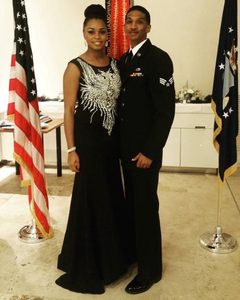 Tamara in a gown and her husband in his dress mess uniform pose in front of flags