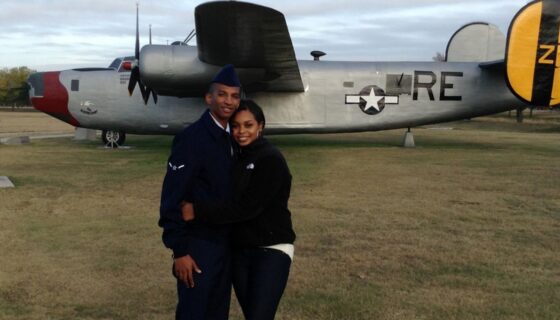 US Air Force spouse Tamara Lynch and her husband in uniform hug in front of a static display of a vintage Air Force plane.