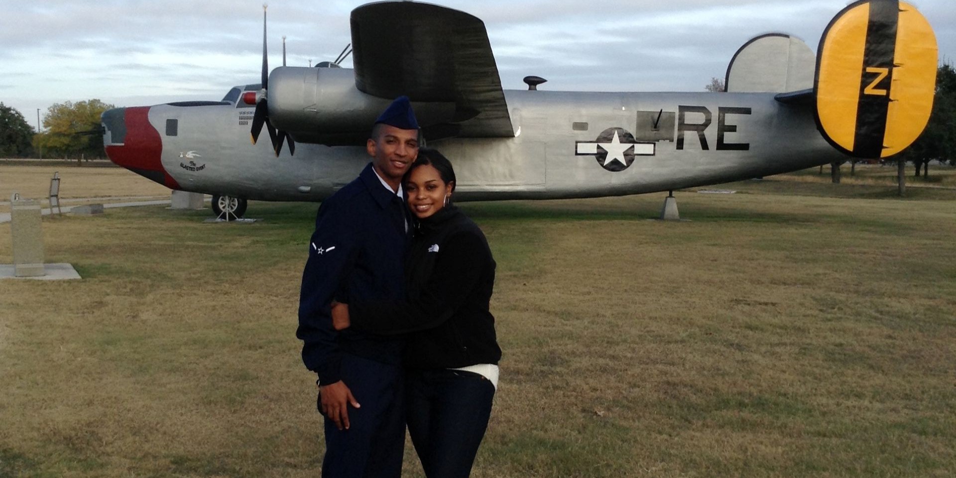 US Air Force spouse Tamara Lynch and her husband in uniform hug in front of a static display of a vintage Air Force plane.
