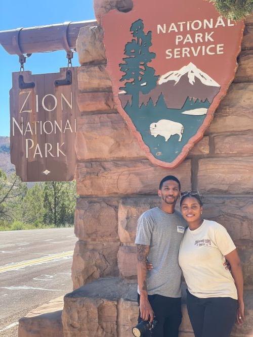 Tamara and her husband posing in front of the Zion National Park sign