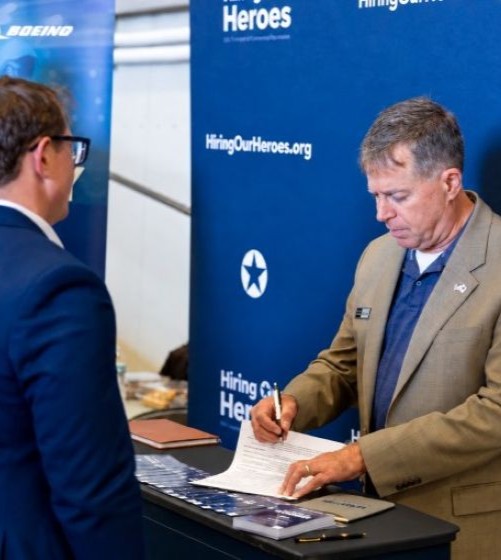 Employer at a hiring event helps a job seeker and records information on a form.